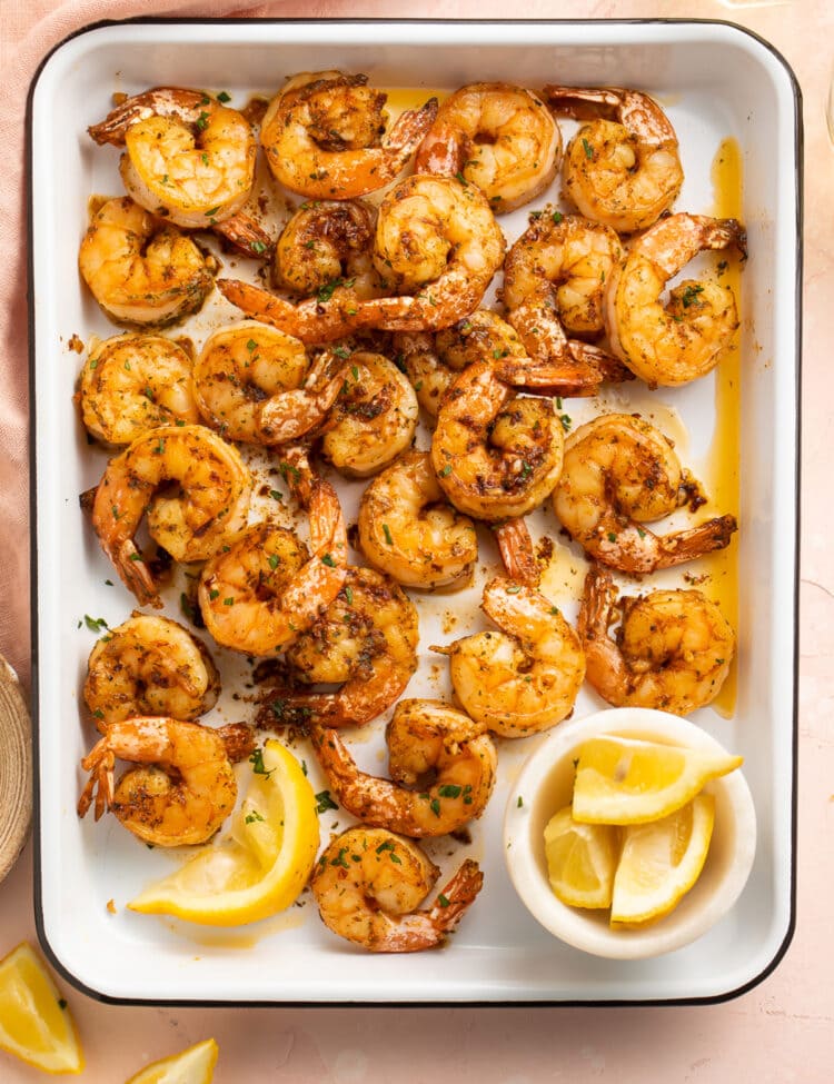 Garlicky, buttery broiled shrimp in a roasting pan on a pink tablecloth.