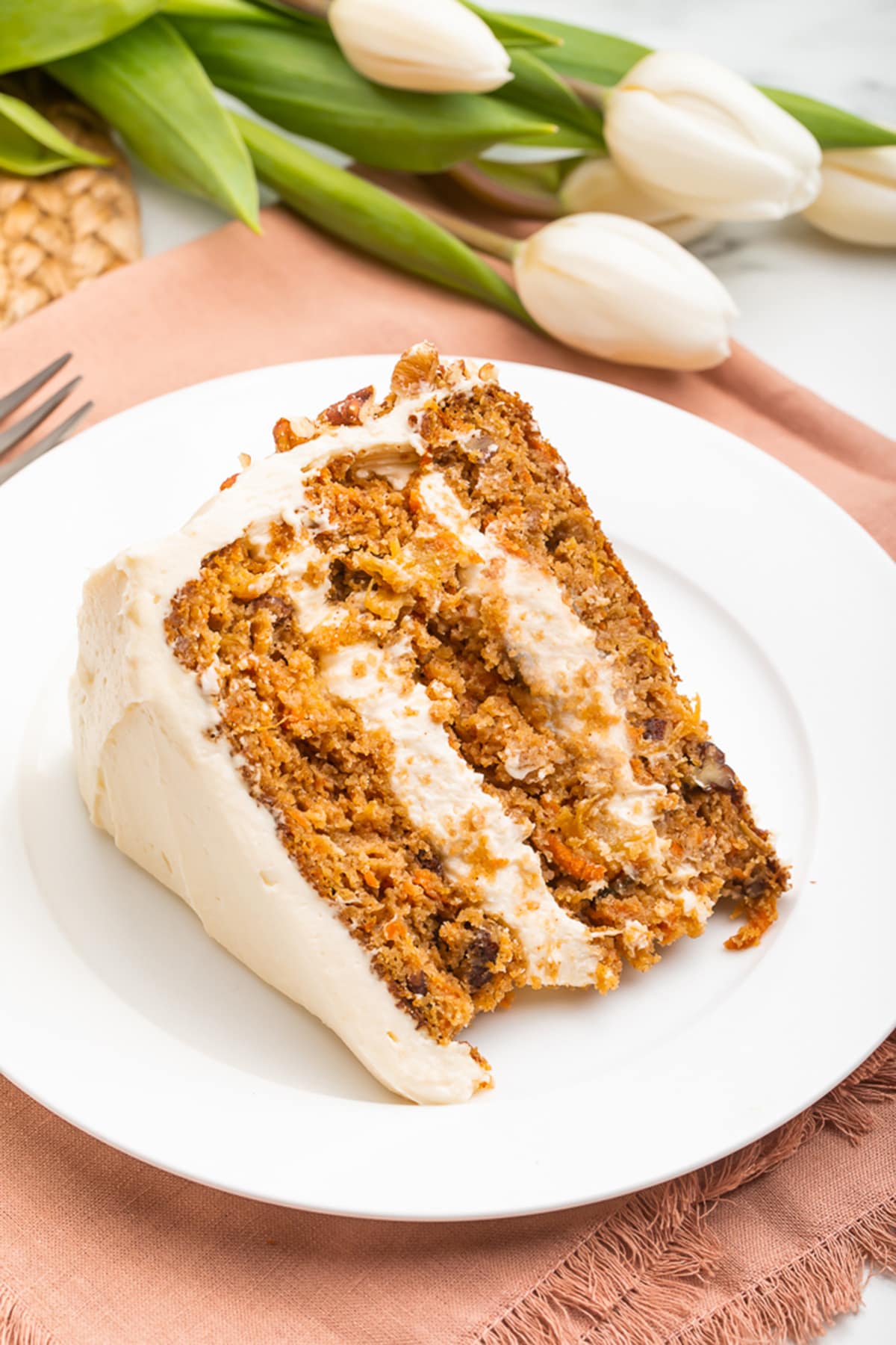Slice of paleo carrot cake on a white plate resting on a light pink cloth napkin.