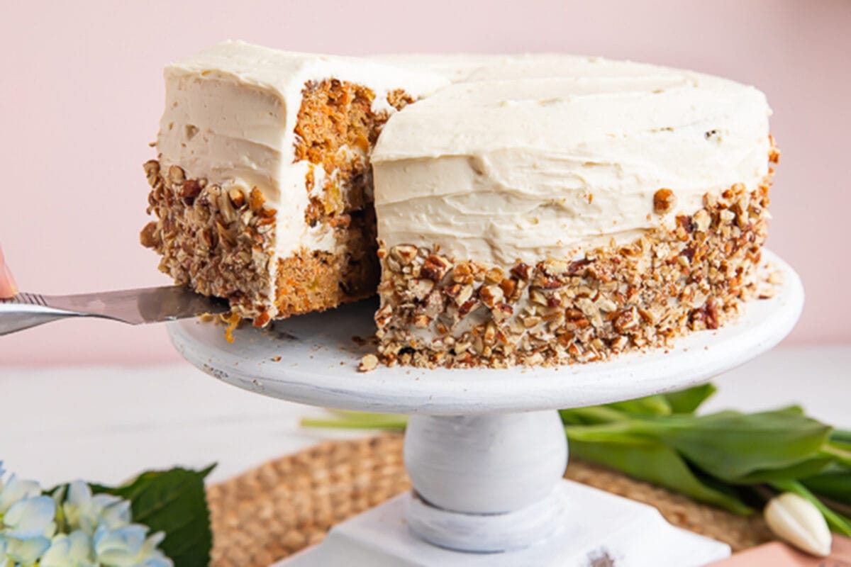 Paleo carrot cake on a cake stand with a piece being lifted out.