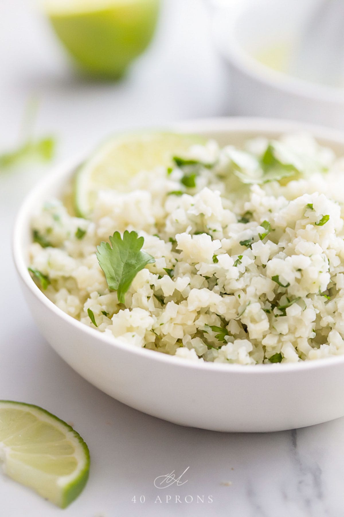 Cilantro lime cauliflower rice, garnished with a lime wedge, in a white bowl on a marble countertop.
