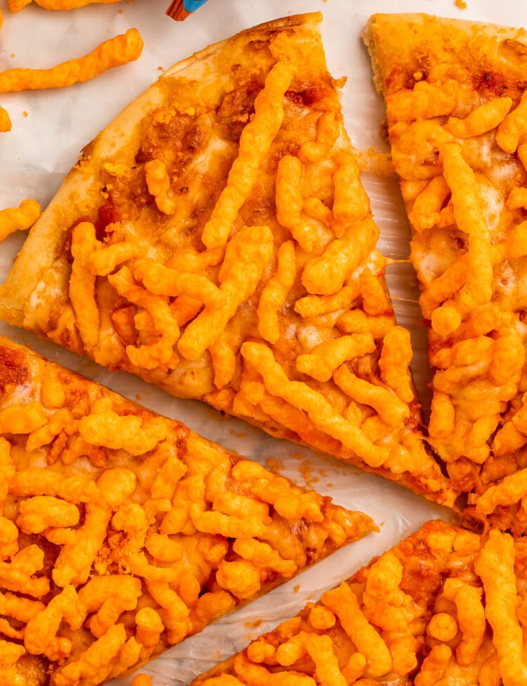 A slice of cheese pizza topped with crunchy Cheetos, being pulled away from other slices of pizza.