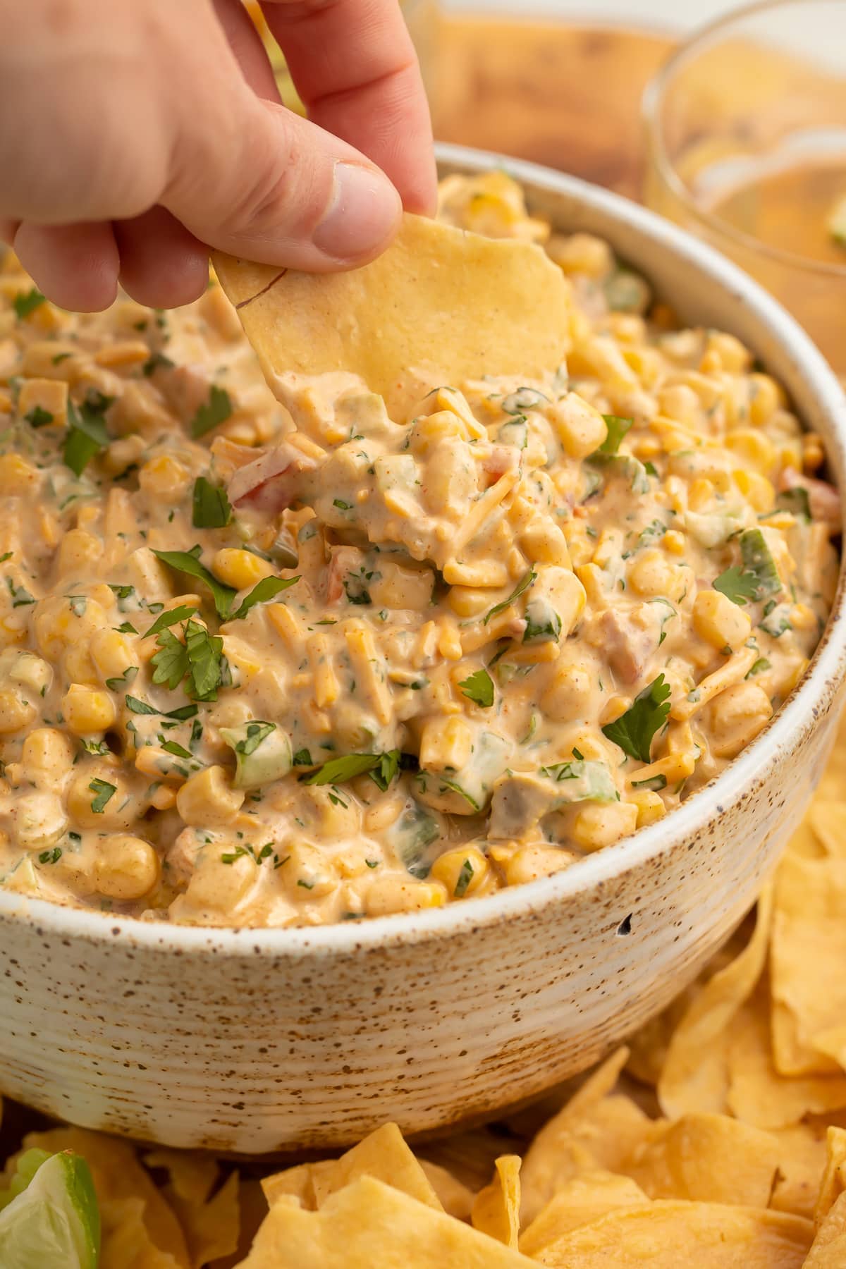 A white woman's hand using a corn chip to scoop a serving of Mexican corn dip out of a bowl.