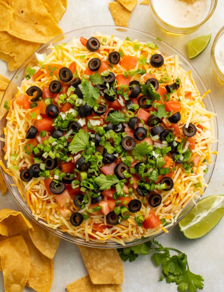Top-down view of a large glass bowl filled with a 7 layer dip topped with green onions and olives.