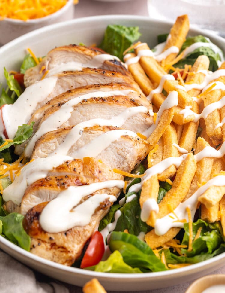 Angled view of a large bowl holding a Pittsburgh chicken salad with french fries and a drizzle of ranch dressing.