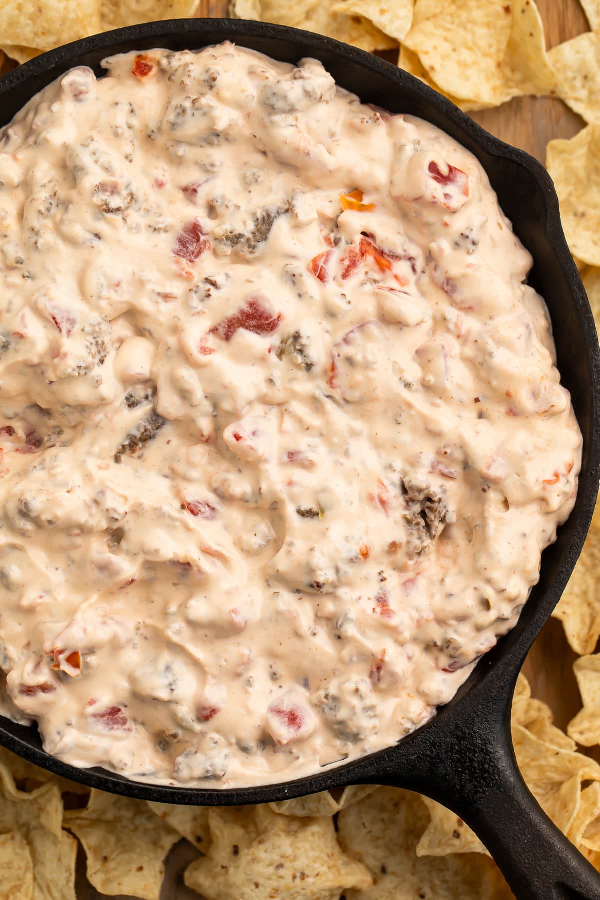 Overhead view of a cast-iron skillet filled with cream cheese sausage dip surrounded by tortilla chip scoops.