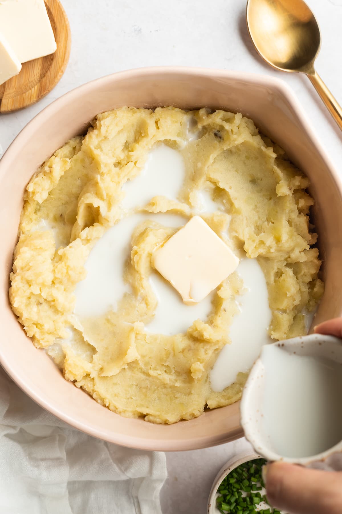 Mashed potatoes topped with butter and milk in a large bowl with a large spoon.
