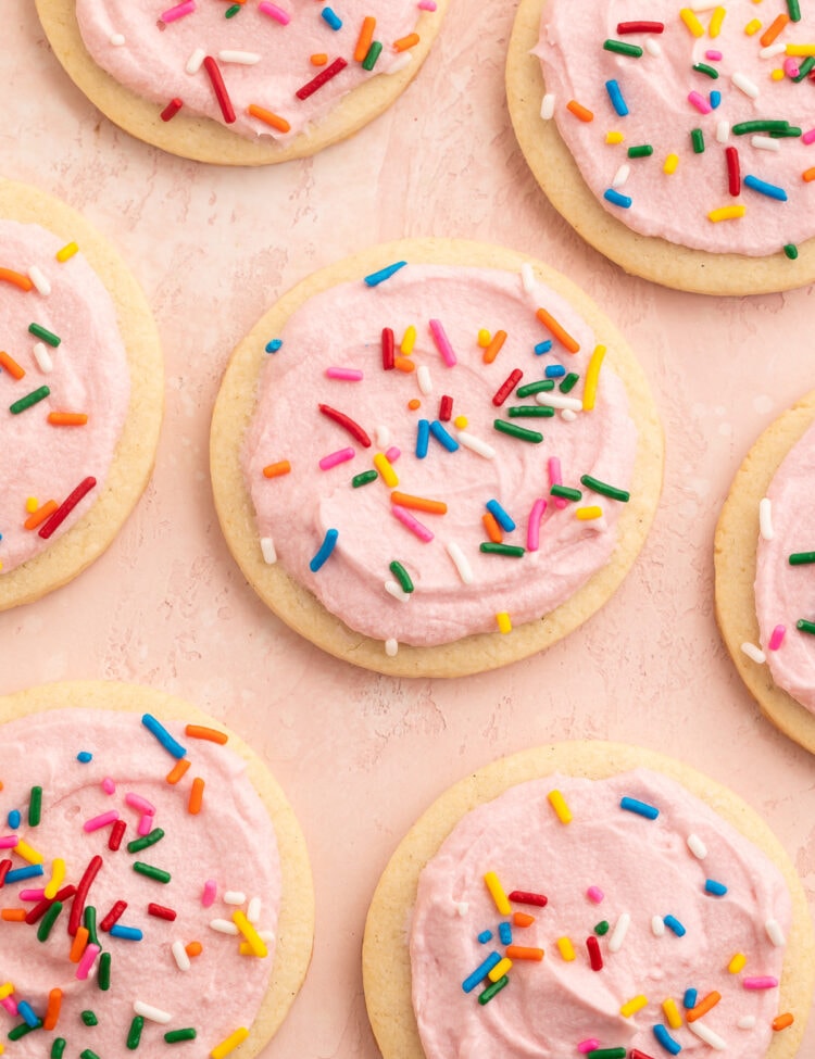 Rows of gluten free sugar cookies topped with pink buttercream frosting and rainbow jimmies on parchment paper.