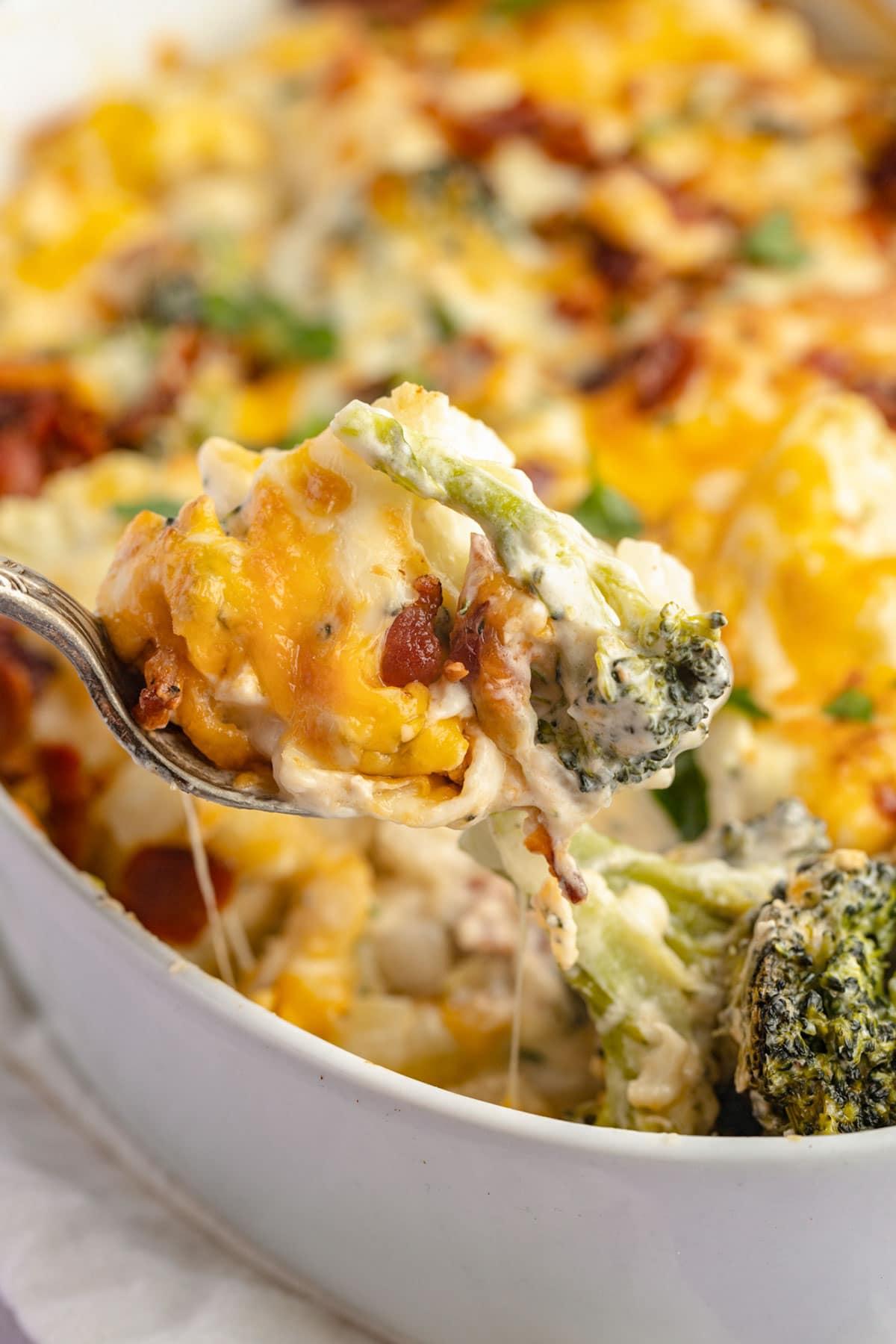 A spoonful of keto broccoli cauliflower casserole being lifted out of a casserole dish.