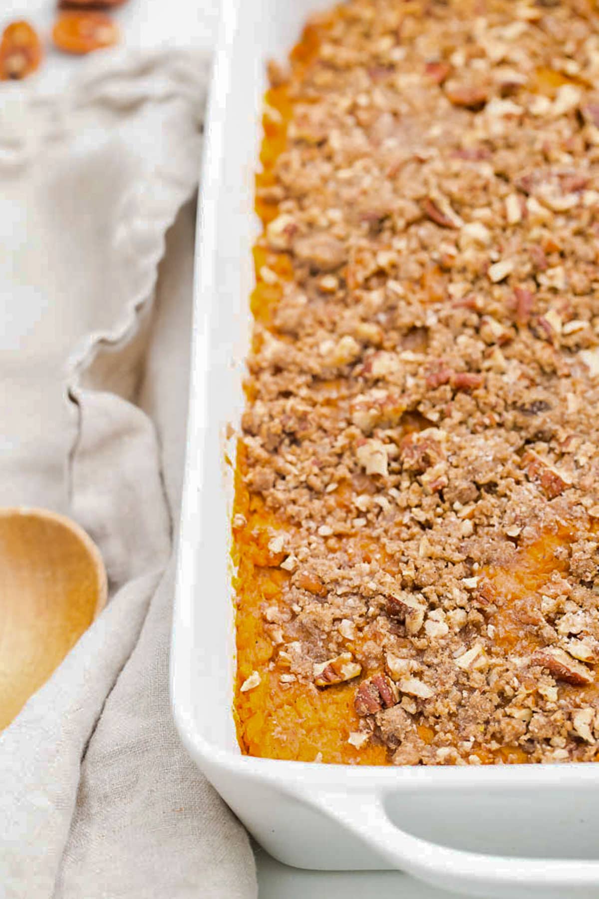 A large white rectangular casserole dish holding sweet potato casserole topped with pecans.