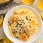 Chicken piccata plated with pasta and capers.