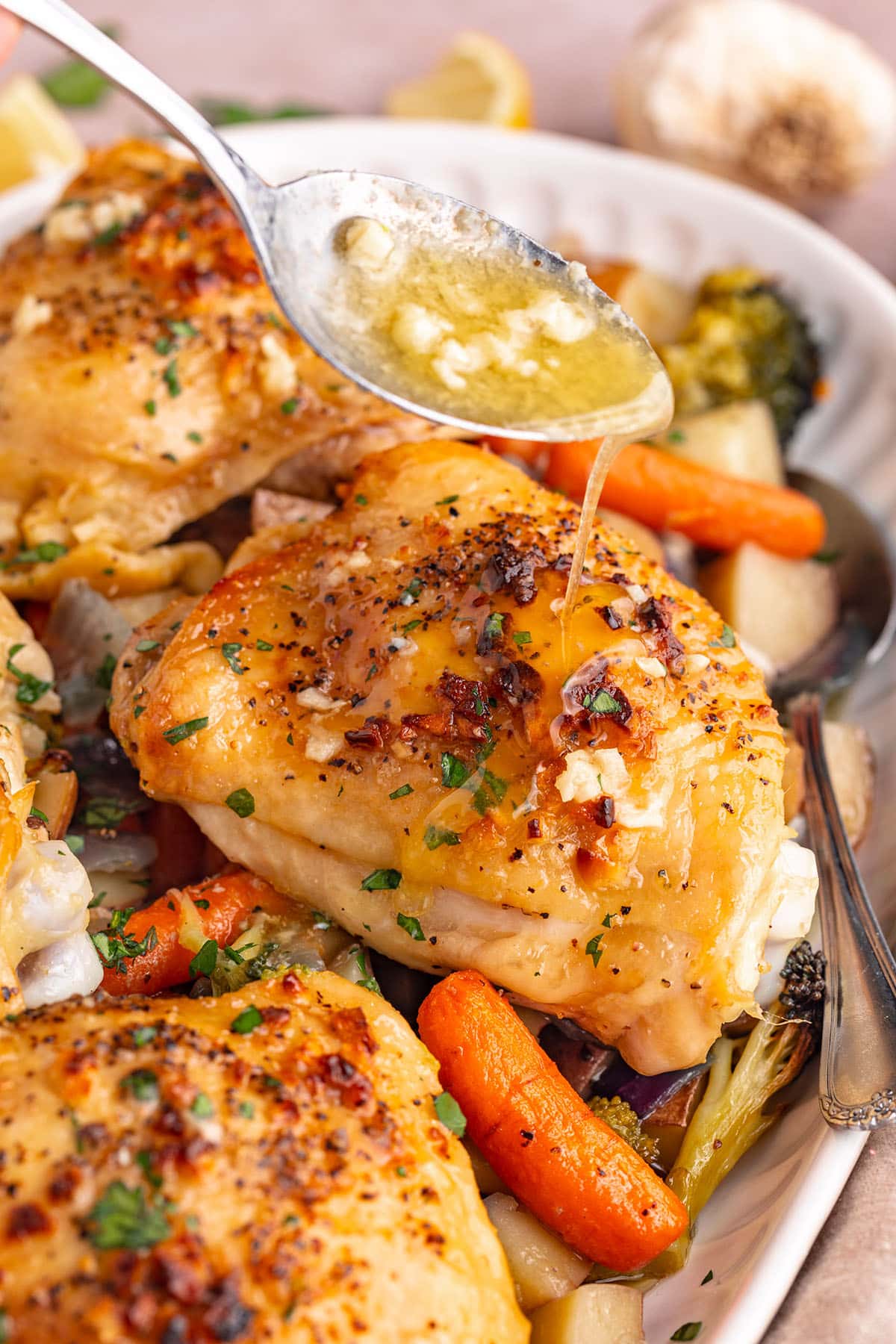 Garlic butter sauce being spooned over a one-pan chicken thigh and oven-roasted veggies.